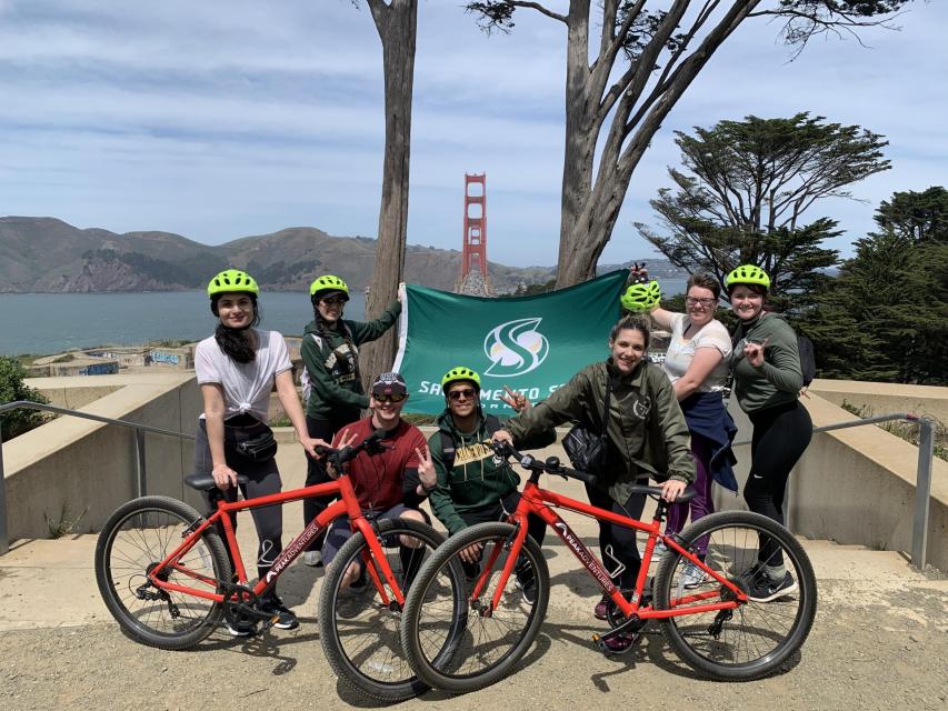 Students from sac state on a peak adventures bike trip to the golden gate bridge in San Francisco with red bikes holding a sac state flag.