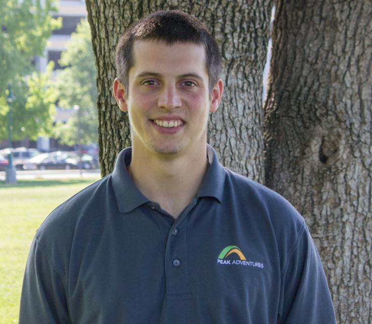 John Gratton in a polo shirt standing in front of a tree.