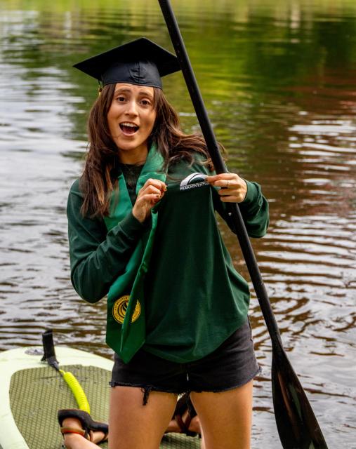 Cindy paddling on the river showing off her peak shirt and wearing her grad gear.