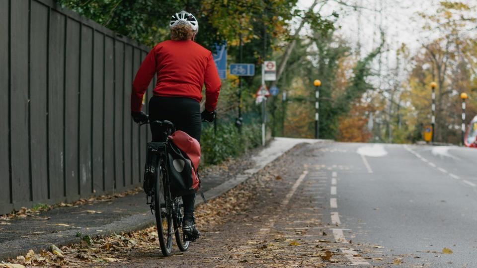 Photo of someone in a red jacket riding their bike in fall.